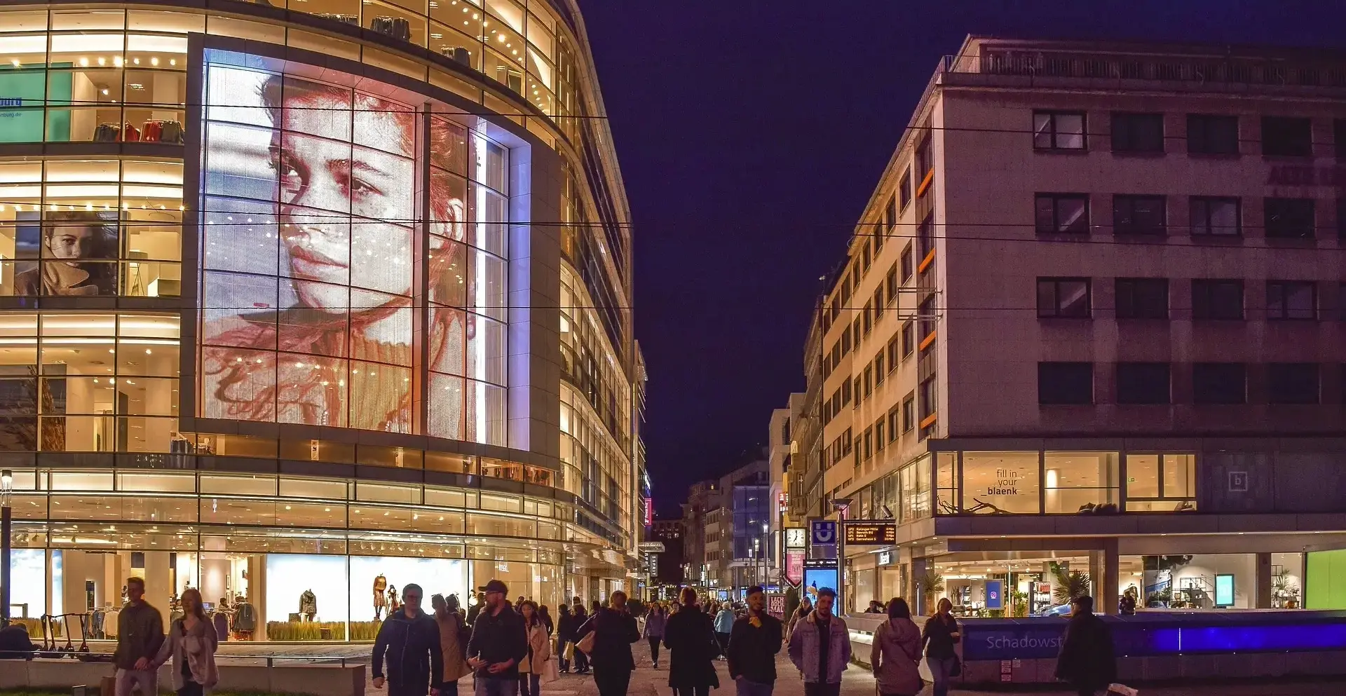 Avenida publicitaria en estilo japonés con múltiples paneles LED coloridos, anuncios llamativos en varios idiomas y ambiente urbano vibrante.
