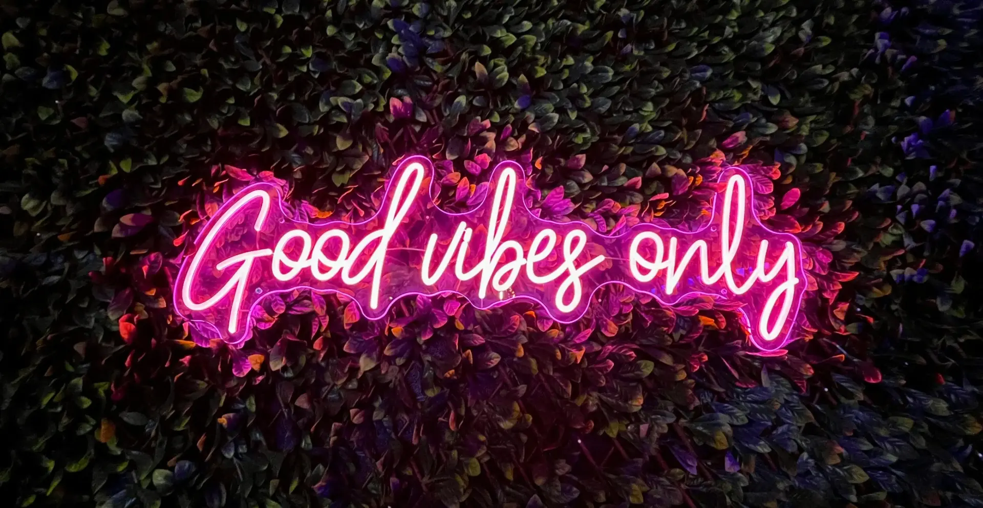 Letrero LED con la frase 'Good vibes only' en luz neón fucsia, sobre fondo verde natural. Diseño moderno, juvenil y perfecto para espacios instagrameables.